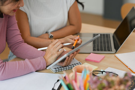 Cropped view businesswomen sitting in an office working on a tablet and a laptop together, for...