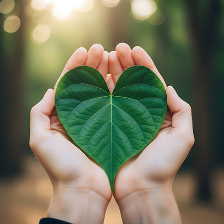 Hands holding green leaf in heart shape on blurred nature background. Ecology conceptの写真素材
