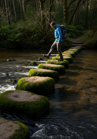 Man walking on stepping stones over a stream in the forest.の写真素材
