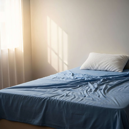 Double bed with pillows and blanket in bedroom at morning sunlight.