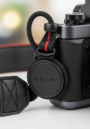 Black digital camera with leather strap on white background, close-up