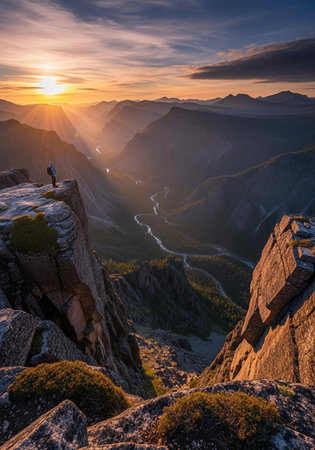 A man stands on top of a mountain and looks at the sunsetの写真素材