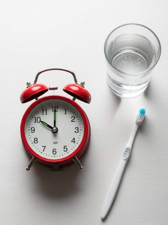 Alarm clock, glass of water and toothbrush on white background