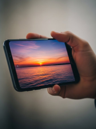 Man taking a photo of the sunset with his mobile phone. Close up