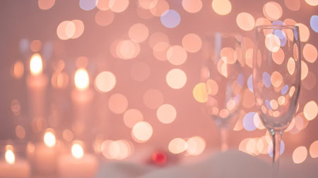 A serene and intimate dinner setting featuring wine glasses, candles, and a blurred background of warm, golden lights, evoking a sense of romance and sophistication.の写真素材