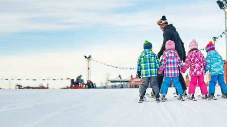 A joyful family of five, dressed in vibrant winter clothing, skis together on a snowy slope, enjoying a fun day outdoors in a festive atmosphere.の写真素材