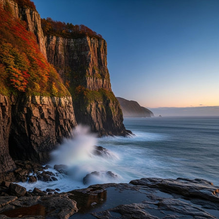 A rugged cliffside meets the ocean at sunset with vibrant autumn foliageの写真素材