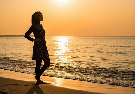 Silhouette of a woman standing on the beach at sunset.の写真素材