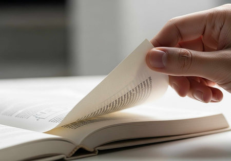 Close-up of a hand flipping the pages of an open book on a table.