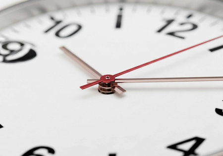 A close-up view of a clock with red and silver hands on a white face, showing the numbers 1-12.