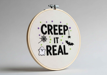 Embroidered hoop art featuring "Creep It Real" text with Halloween icons: ghost, spider web, bat, and polka dots.の写真素材