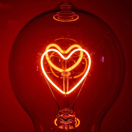 A glowing red light bulb with a heart-shaped filament insideの写真素材