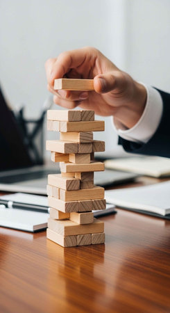 A person in a business suit carefully building a tower with wooden blocks on a desk in an officeの写真素材