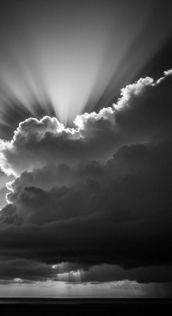 A dramatic black and white photo of sun rays shining through dark clouds