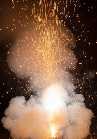 A vibrant firework explodes in the night sky with a burst of light and smoke