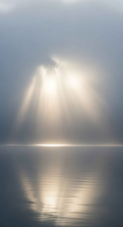 Sunlight beams through fog, illuminating a serene body of water with reflective surfaces.