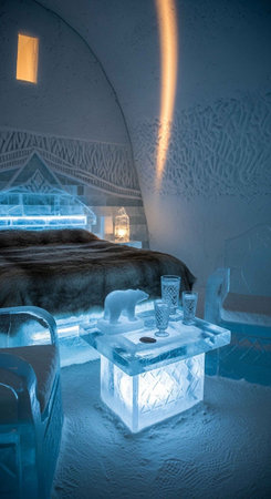 Elegant ice hotel room featuring a bed with fur coverings, ice sculptures, and ambient lighting.