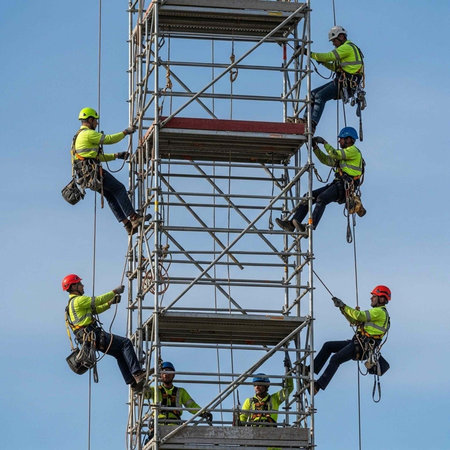 A group of construction workers climbing a scaffolding tower with safety gear