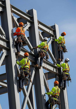 A group of construction workers climbing a large metal structure in a clear blue skyの写真素材
