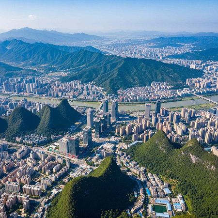 Aerial view of a city nestled between mountains and greenery under a clear blue skyの写真素材