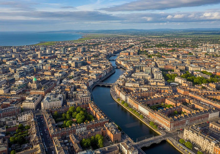 Aerial view of a city with a river flowing through it, surrounded by numerous buildings and trees under a blue sky with clouds.の写真素材