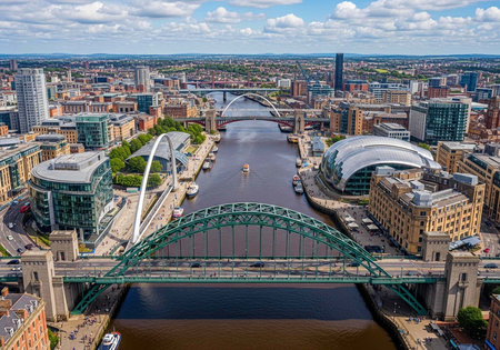 Aerial view of a city with a river flowing through it, featuring multiple bridges, modern buildings, and a mix of green spaces and urban landscape under a cloudy blue sky.の写真素材