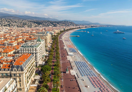 Aerial view of a coastal city with a long beach, lined with buildings, palm trees, and colorful umbrellas, with boats in the ocean and mountains in the background.の写真素材