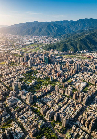 Aerial view of a city with skyscrapers, greenery, and mountains in the background under a clear blue skyの写真素材
