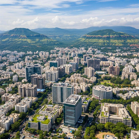 Aerial view of a city with modern buildings, green spaces, and mountains in the background under a blue sky with clouds.の写真素材