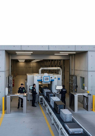 Workers operate security equipment at industrial checkpoint with conveyor belt and metal detectors