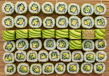 Sushi rolls with avocado and rice on a bamboo mat, accompanied by sliced avocado