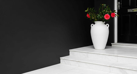 A white vase with red roses sits on the steps of a modern home with a black doorの写真素材