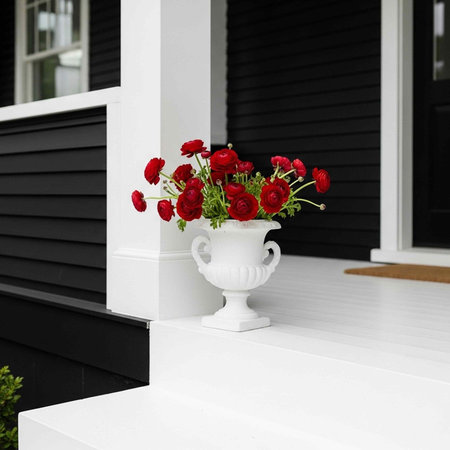 A beautiful white vase with red flowers on a black and white house porch
