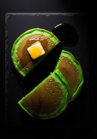 A plate of green pancakes with butter and syrup on a black slate backgroundの写真素材