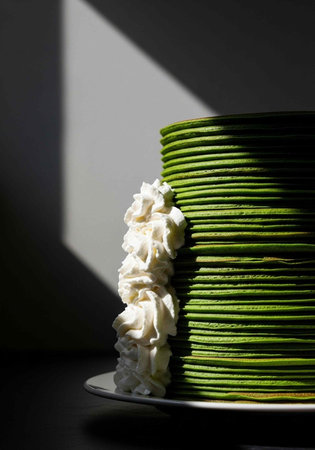 A tall stack of green pancakes with whipped cream on a white plate in a dark room with sunlight...
