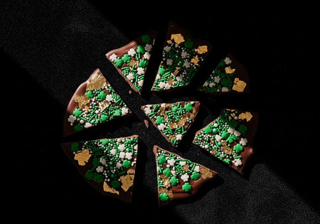 A delicious chocolate cake with green and white sprinkles cut into slices on a black background