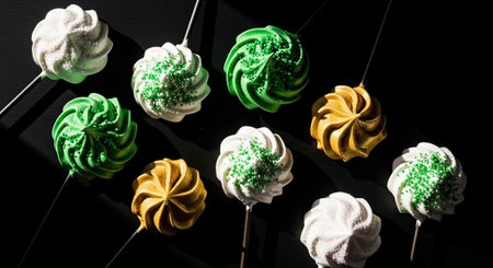 A colorful arrangement of cake pops with white, green, and gold frosting on a black background
