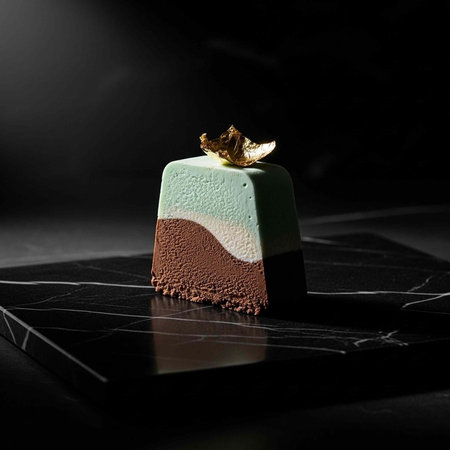 A beautifully styled dessert with a layered design and gold leaf garnish on a dark background