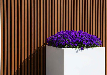 White planter with vibrant purple flowers against brown wooden slatted wall in sunlight