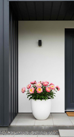 A white planter with pink flowers sits on a gray tile porch of a modern home.の写真素材