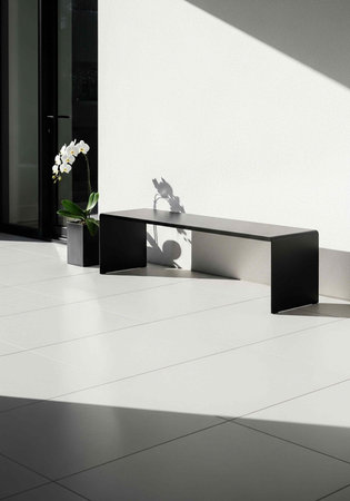 A black bench and white orchid in a modern, minimalist room with sleek floor tiles and sunlightの写真素材