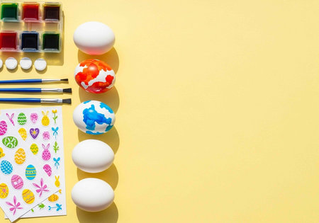 A creative Easter setup with eggs, paints, and brushes on a yellow backgroundの写真素材