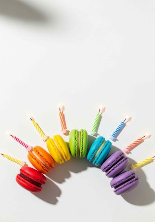 Vibrant macarons in rainbow colors with lit candles on a clean white surfaceの写真素材
