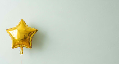 A shiny gold star-shaped balloon tied to a string against a plain light gray wall.の写真素材