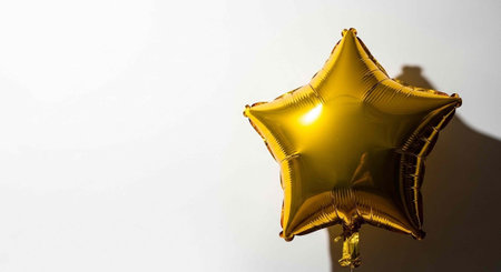 A shiny gold star-shaped balloon with a shadow on a plain white wall.の写真素材