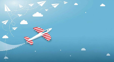 A small white airplane with red stripes flies through a blue sky with white clouds and paper...