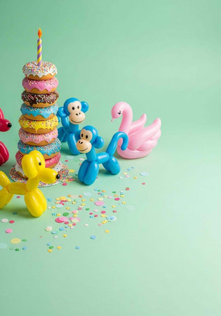 A colorful birthday scene with balloons and donuts on a green background