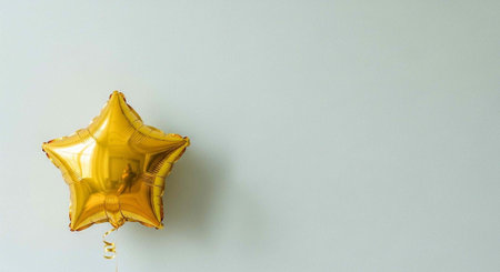 A shiny gold star-shaped balloon tied to a string against a plain light gray wall.の写真素材