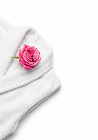 A folded white bathrobe with a pink rose on a clean background for spa and relaxation concepts