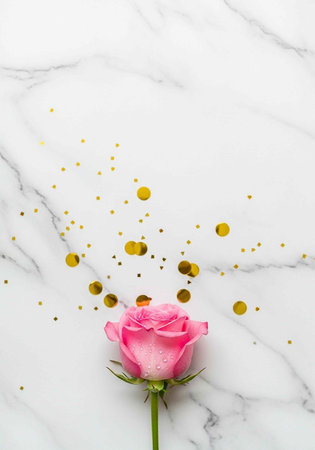 A pink rose on a marble background with gold confettiの写真素材